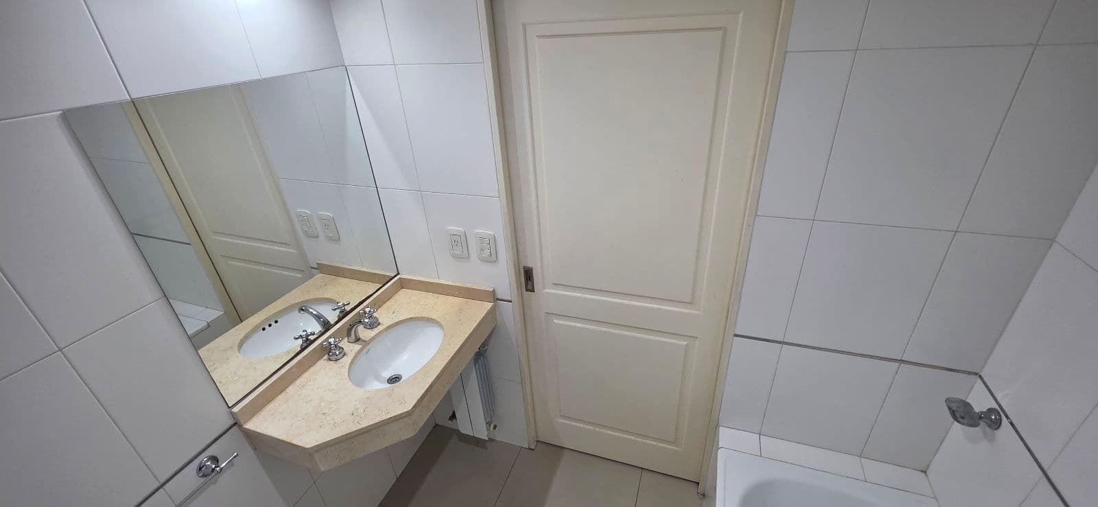 Baño con vanitory, espejo grande y puerta de madera, todo en tonos claros.