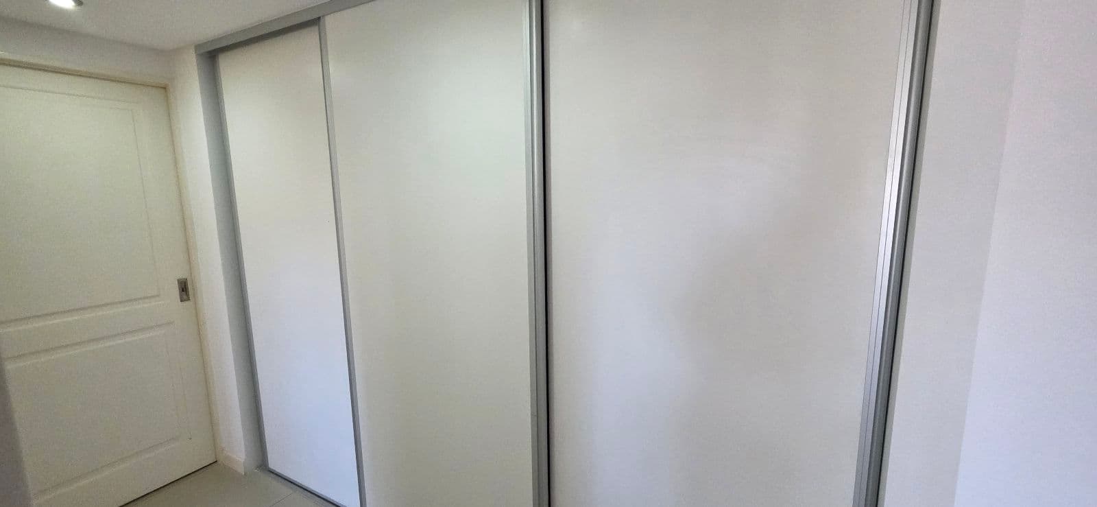 Placard de puertas corredizas blancas en un pasillo junto a una puerta.