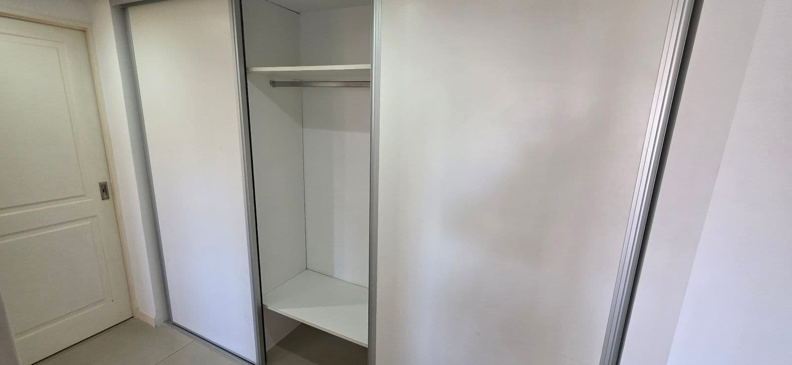 Interior de un placard con barral y estantes, en un pasillo.