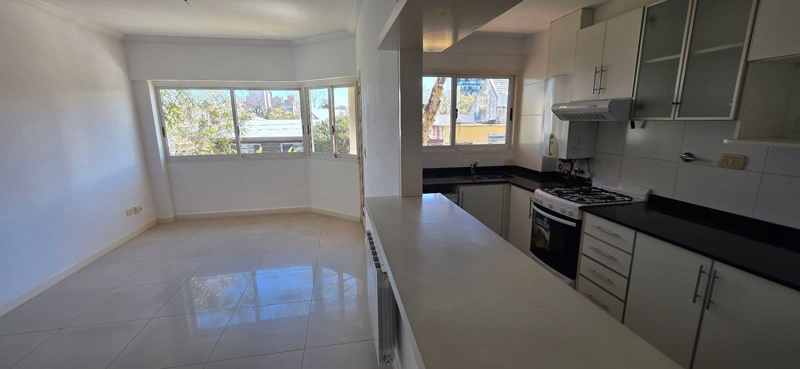 Cocina integrada con mesada oscura, muebles blancos y anafe, junto a ventanales.