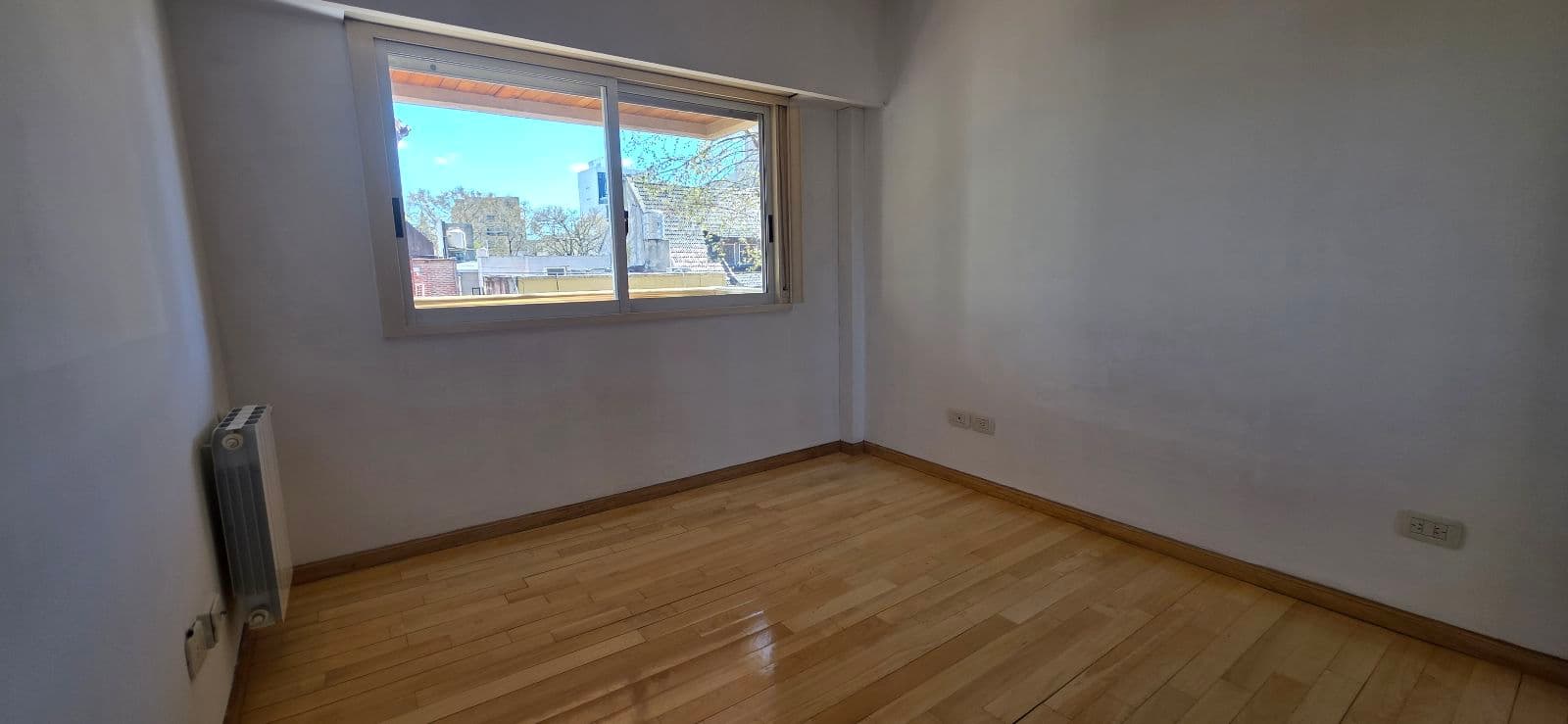 Dormitorio vacío con piso de madera clara y una ventana grande.