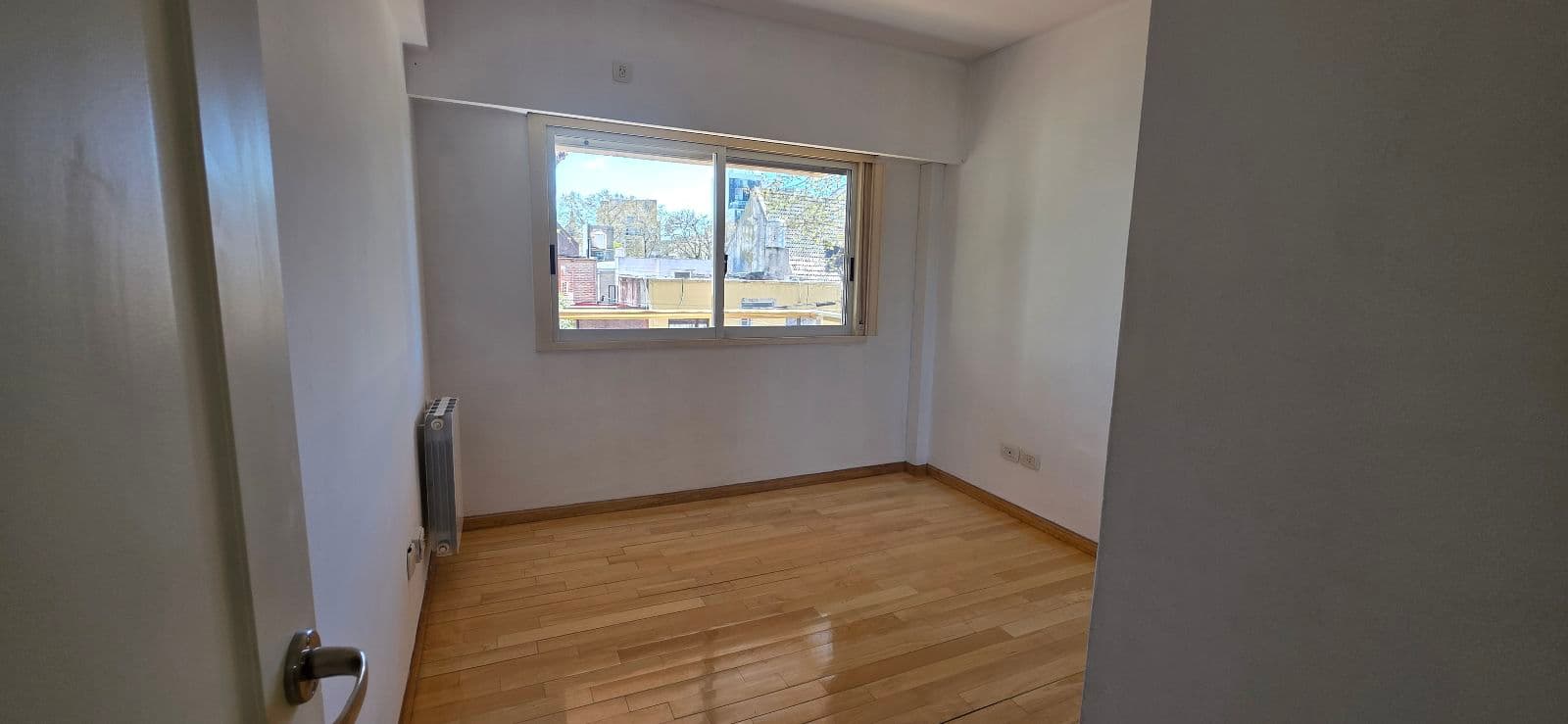 Dormitorio vacío con piso de madera y ventana con vista al exterior.