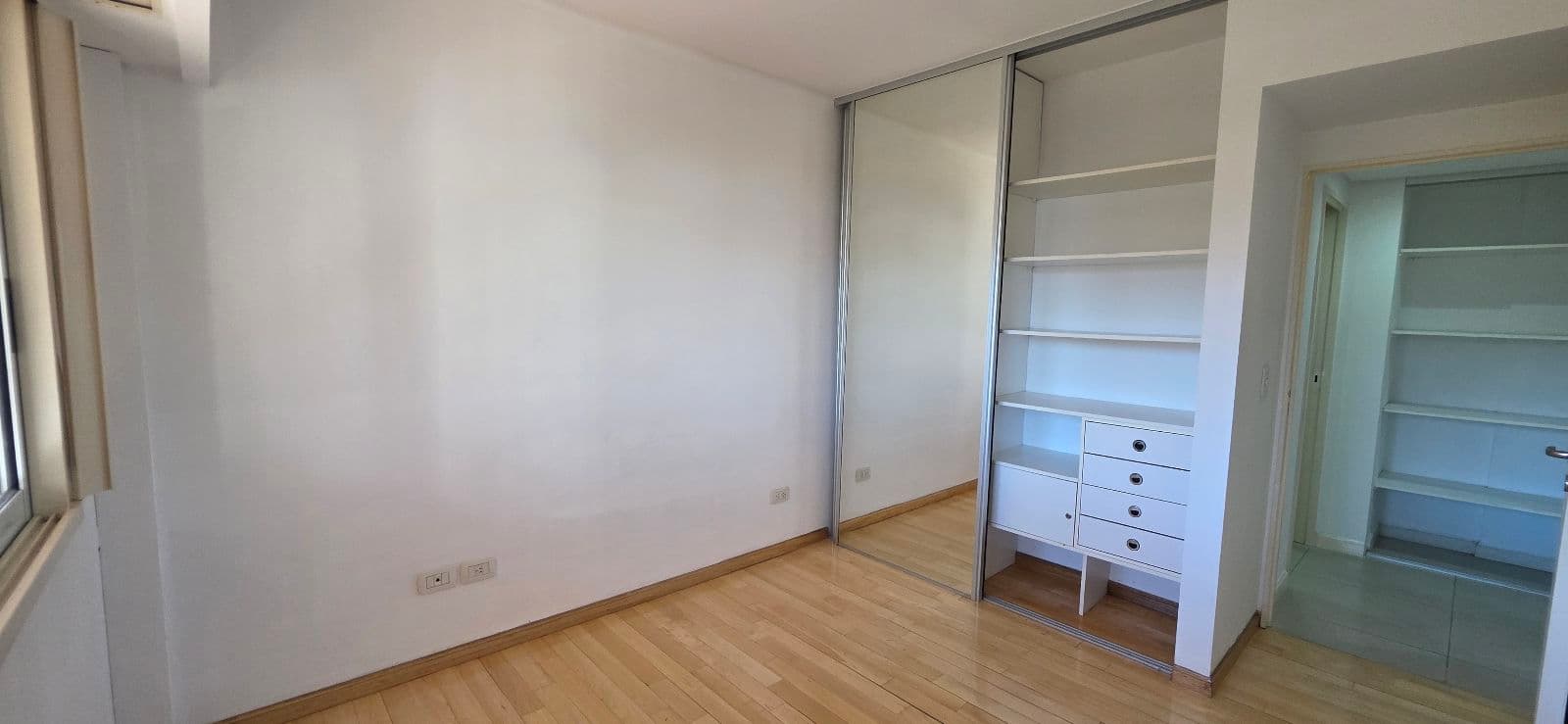 Dormitorio vacío con placard de puertas espejadas y piso de madera.