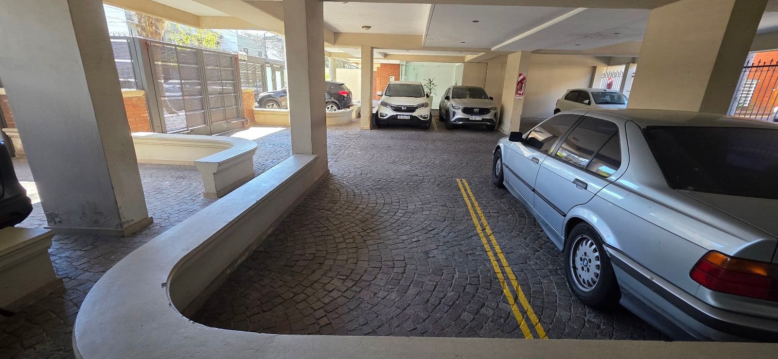 Cochera cubierta con varios autos estacionados, con piso de adoquines.