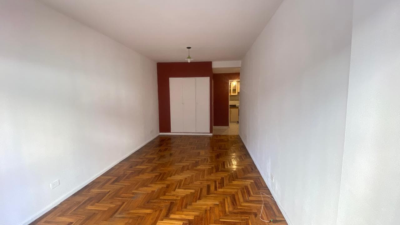 Living vacío con piso de parquet, pared de color y puerta de placard.