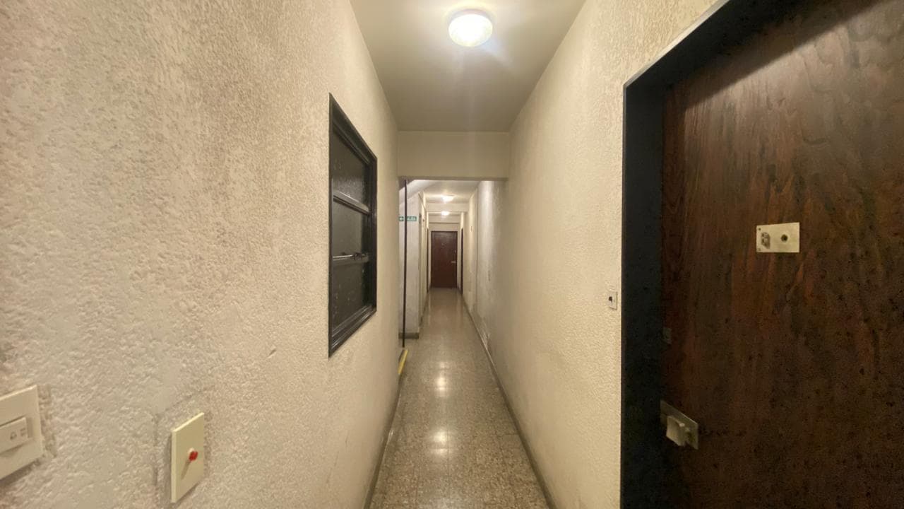 Pasillo oscuro con puerta de madera y ventana.