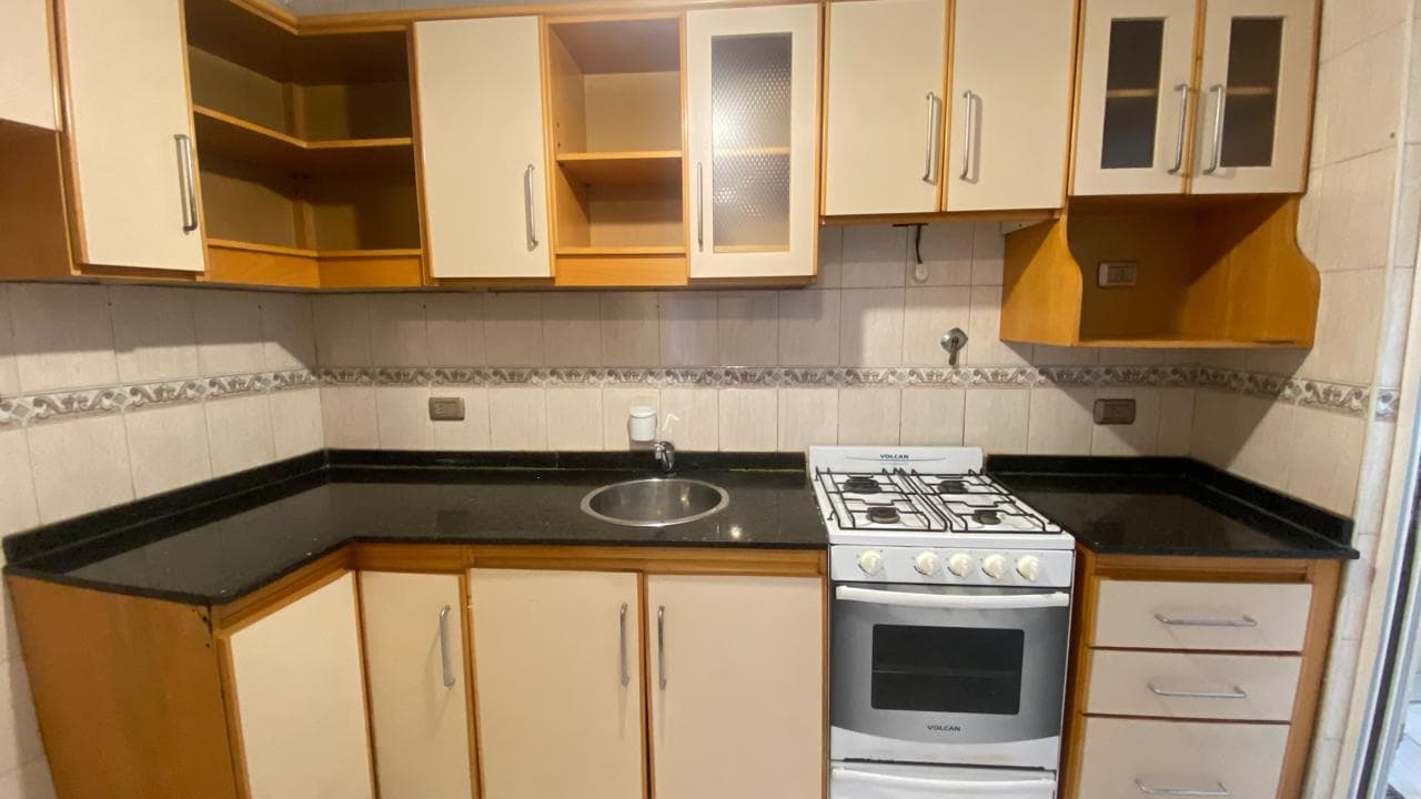 Cocina con mesada negra, bacha, anafe y alacenas de madera y crema.