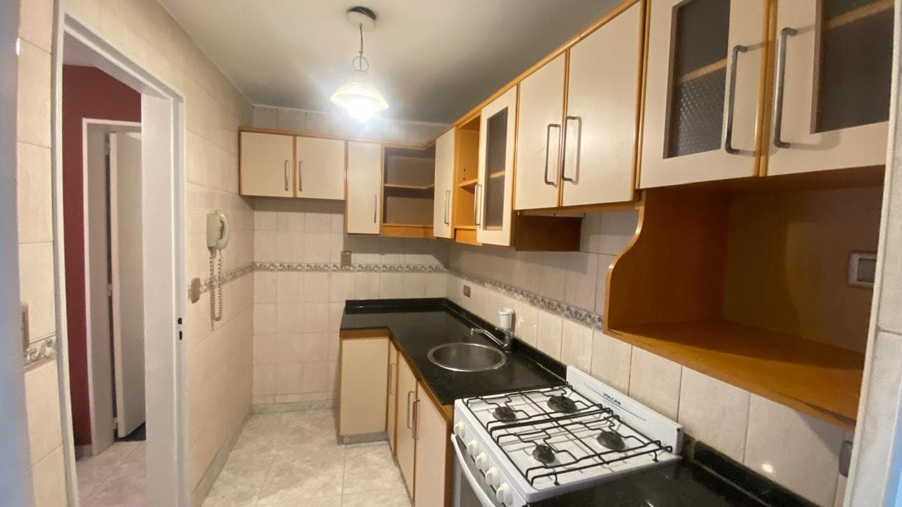 Cocina con mesada, bacha, anafe, alacenas de madera y vista al pasillo.