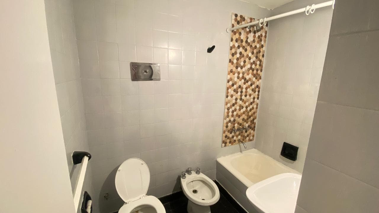 Baño con bañera, inodoro, bidet y azulejos grises y hexagonales.