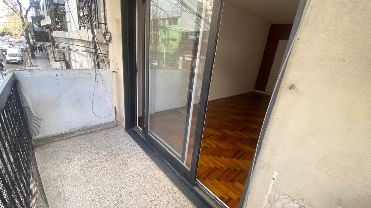 Balcón con piso de baldosas y reja, y vista al interior del departamento.