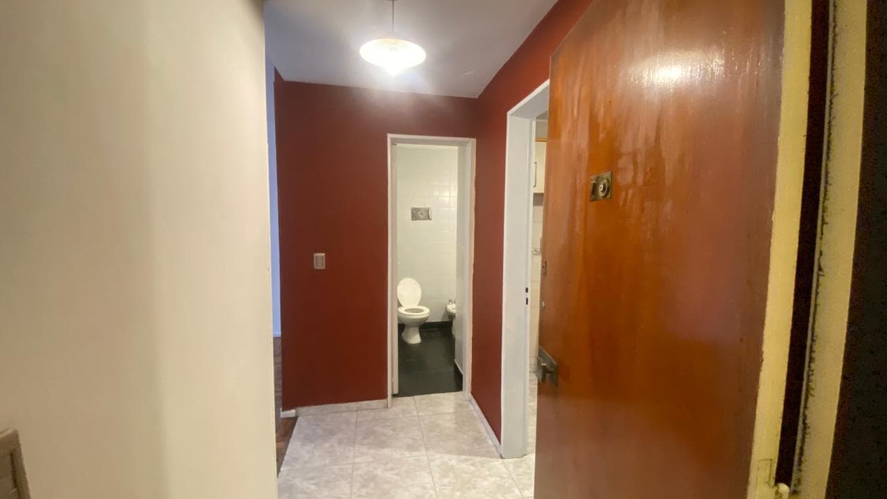 Pasillo de entrada con piso de baldosas, paredes rojas y vista al baño.