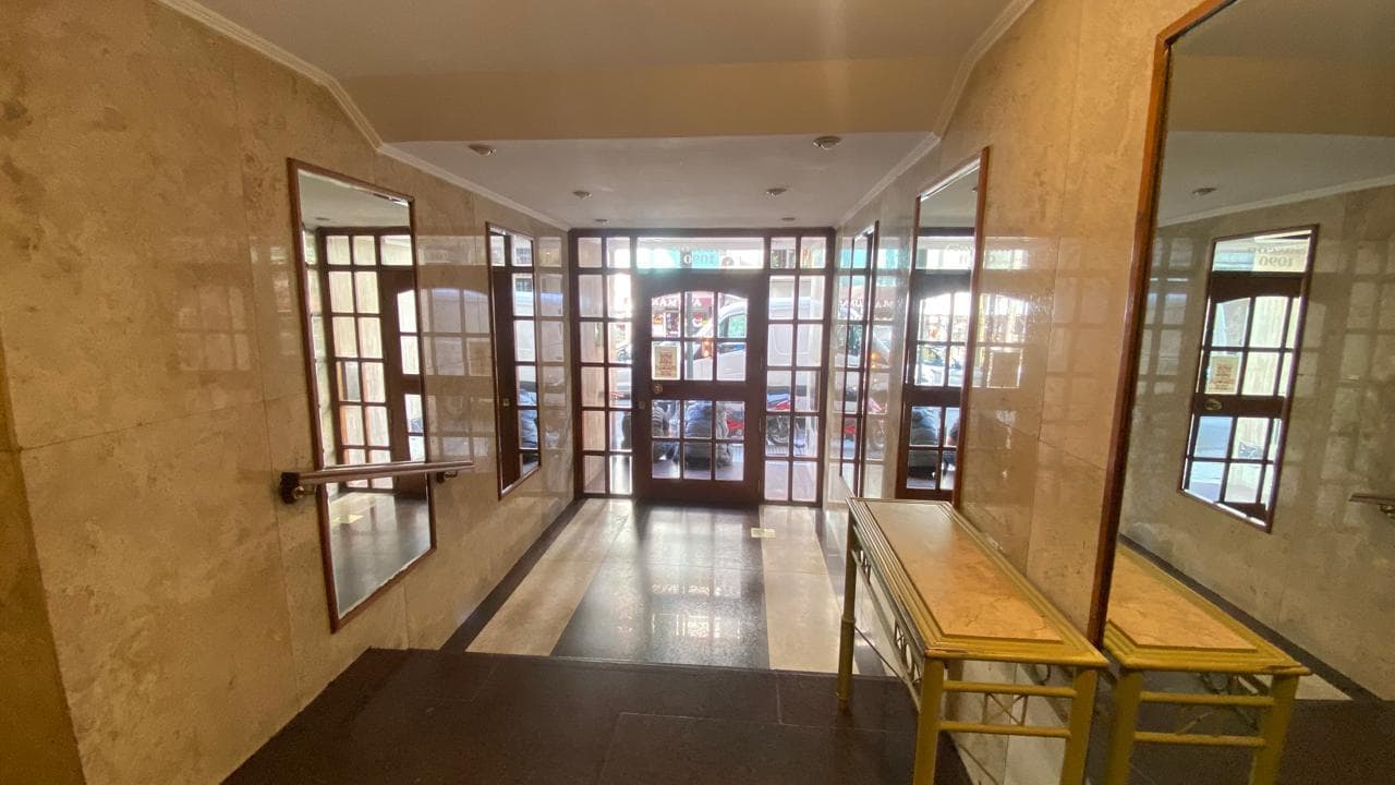 Hall de entrada del edificio con espejos, puerta vidriada y mostrador.