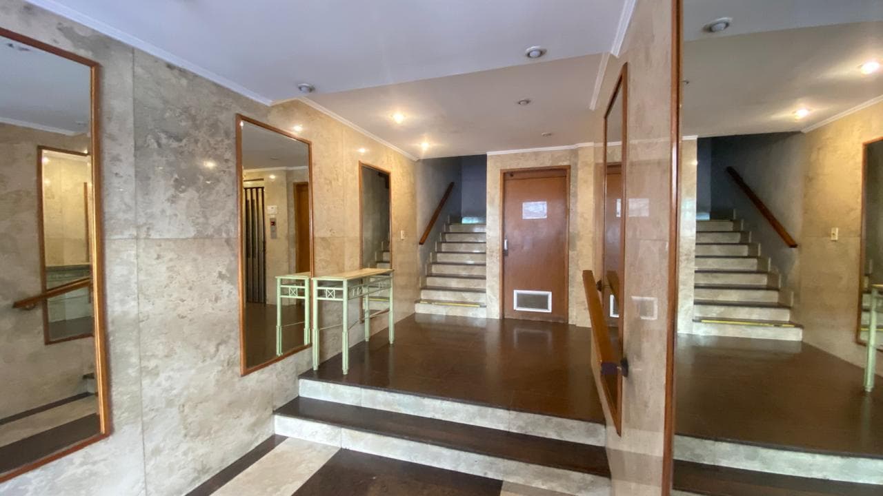 Hall del edificio con escaleras, espejos y un mueble.