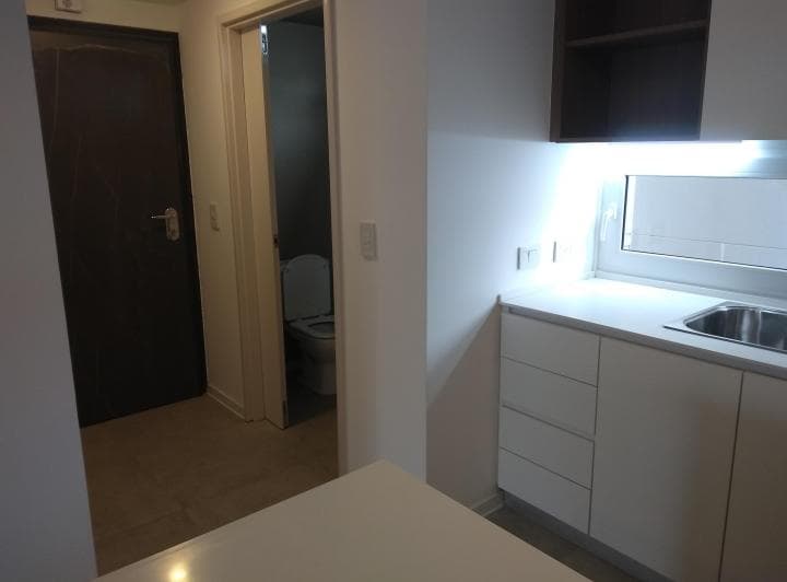 Cocina con muebles blancos y ventana, se ve un inodoro al fondo.