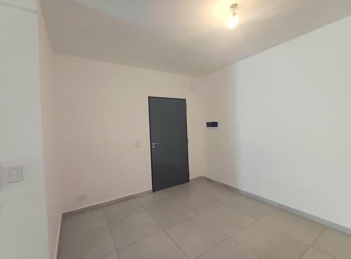 Cuarto vacío con puerta y paredes blancas, piso de baldosas grises.