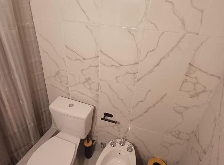 Baño completo con inodoro, bidet y azulejos marmoleados, cortina de ducha.