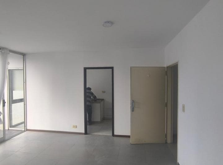 Living vacío con puerta a la cocina, puerta de entrada y puerta ventana.