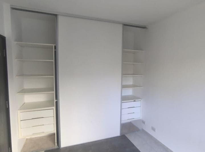 Dormitorio con placard abierto, estantes y cajones, paredes blancas.