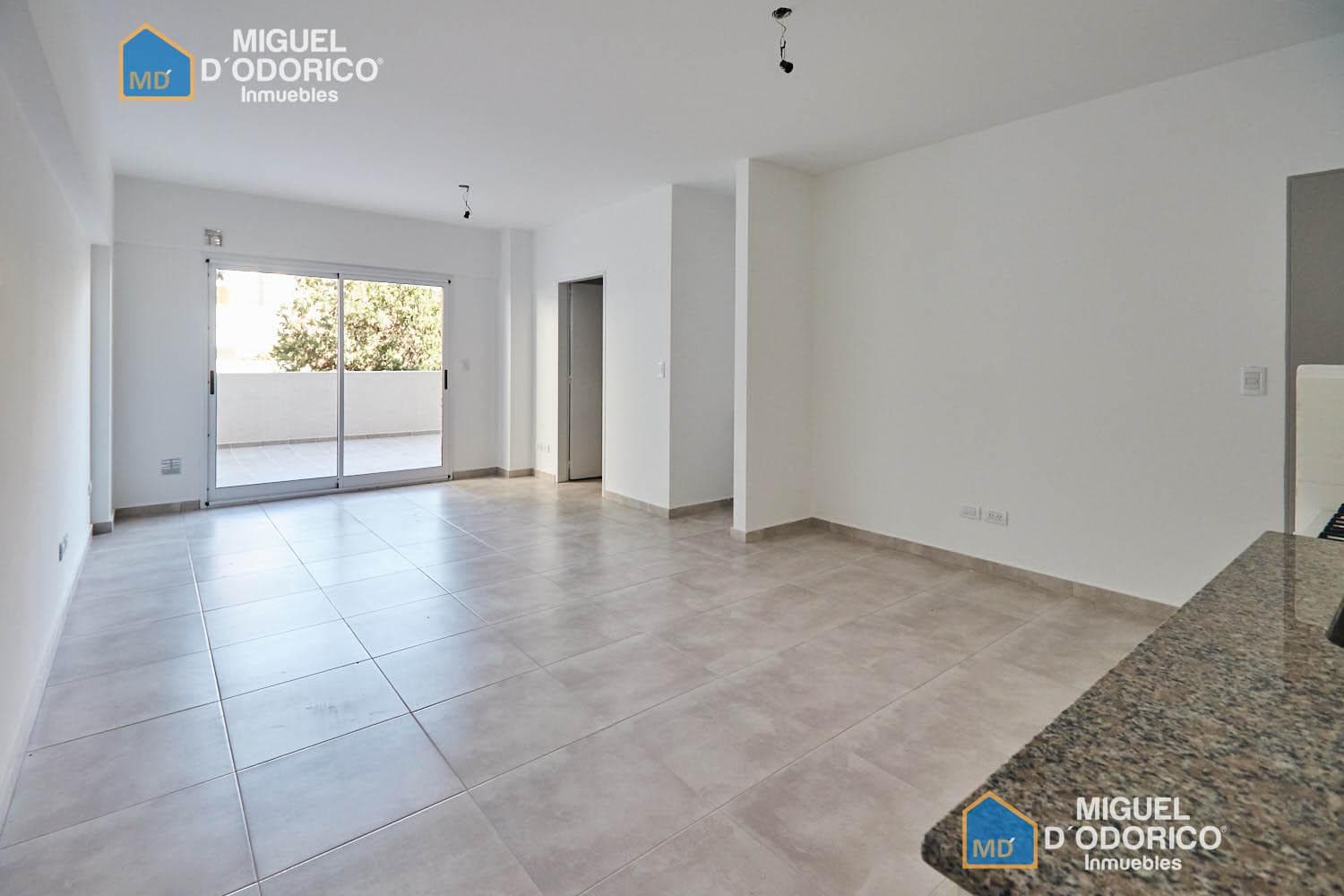 Living vacío con piso de cerámica y puerta balcón.