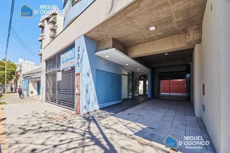 Entrada al edificio con cocheras y cartel de inmobiliaria.