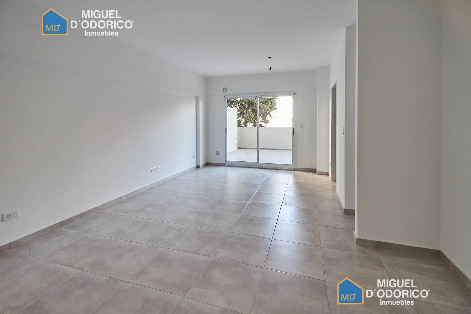 Living vacío con piso de cerámica y acceso al balcón.