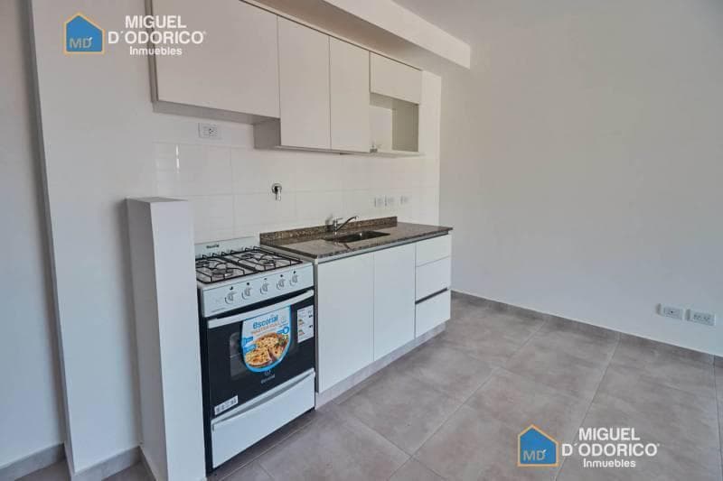 Cocina con anafe, horno, mesada y alacenas blancas.