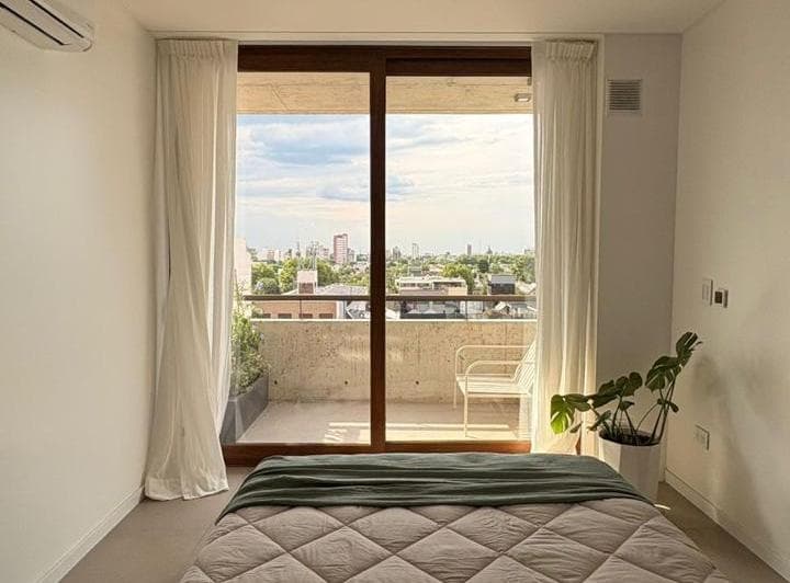 Dormitorio con cama y salida a balcón con vista a la ciudad.