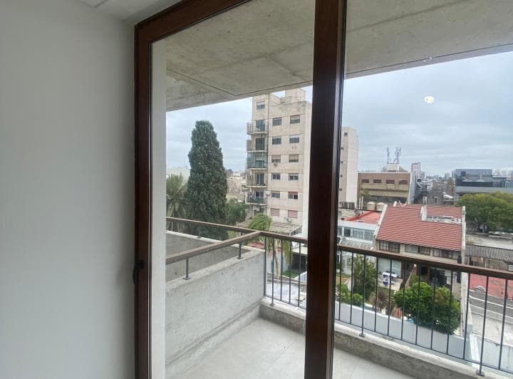 Balcón con ventanal de madera y vista a la ciudad y árboles.