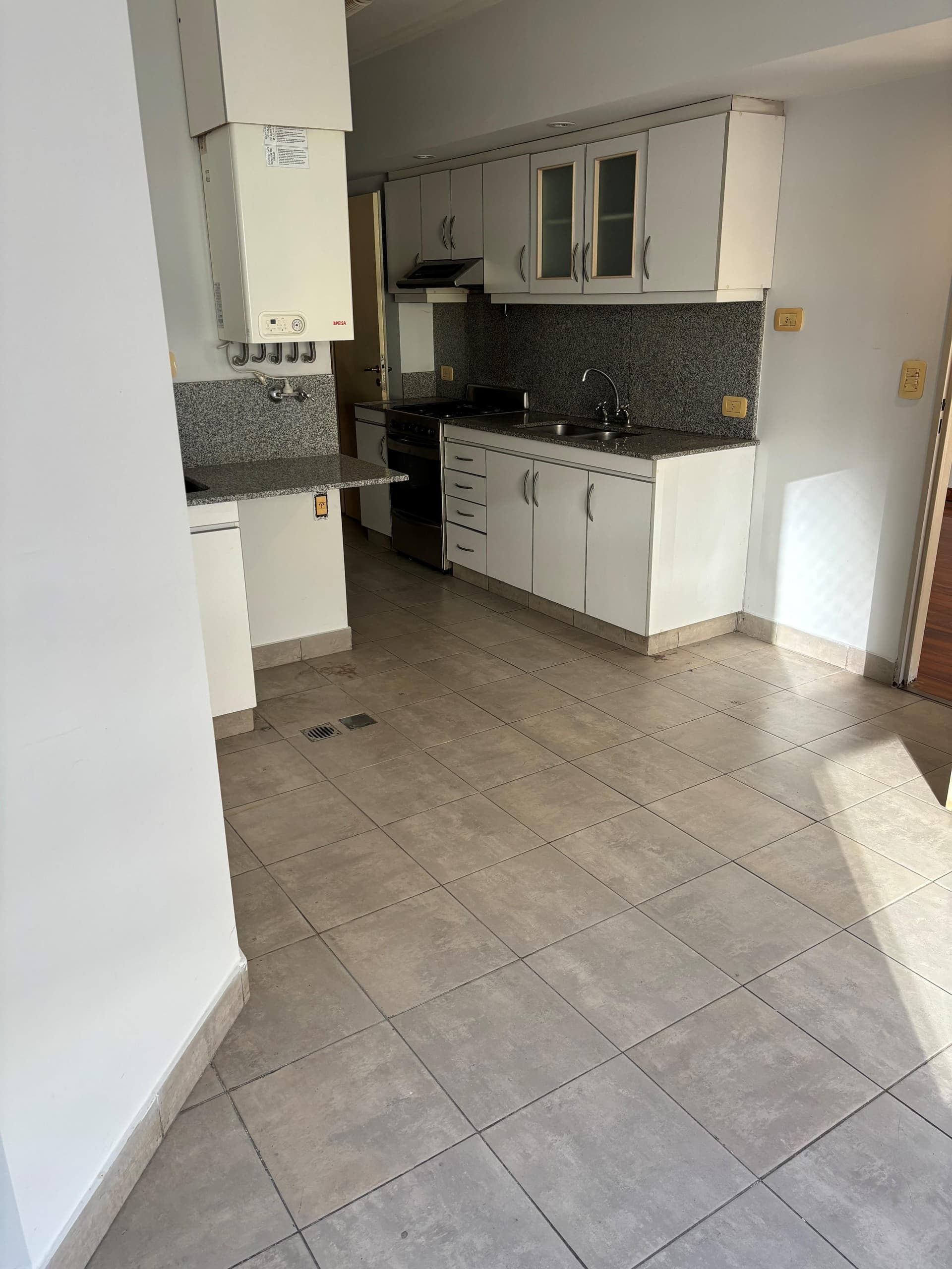 Cocina amplia con muebles blancos y termotanque.