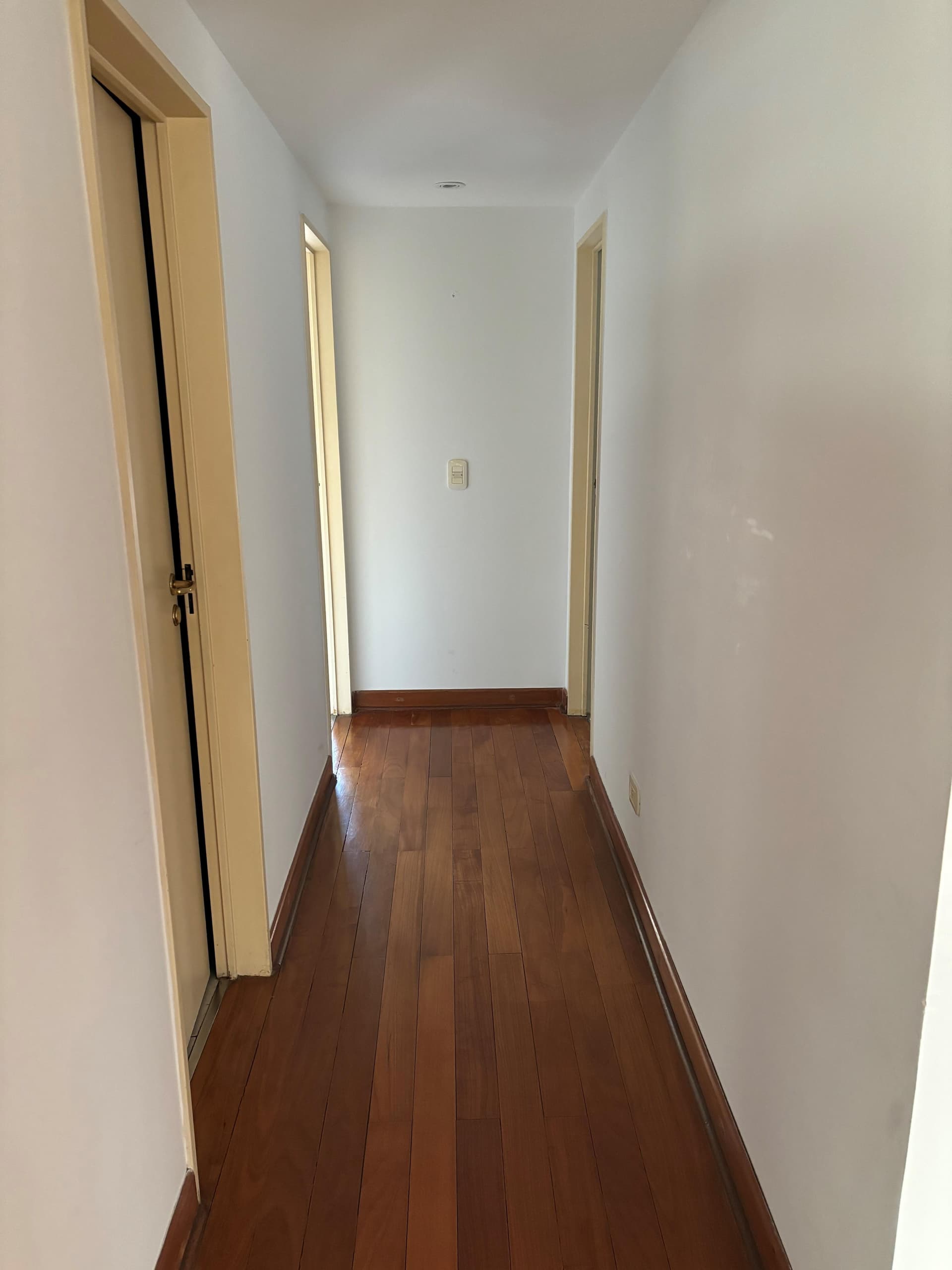 Pasillo interior con piso de madera y paredes blancas.