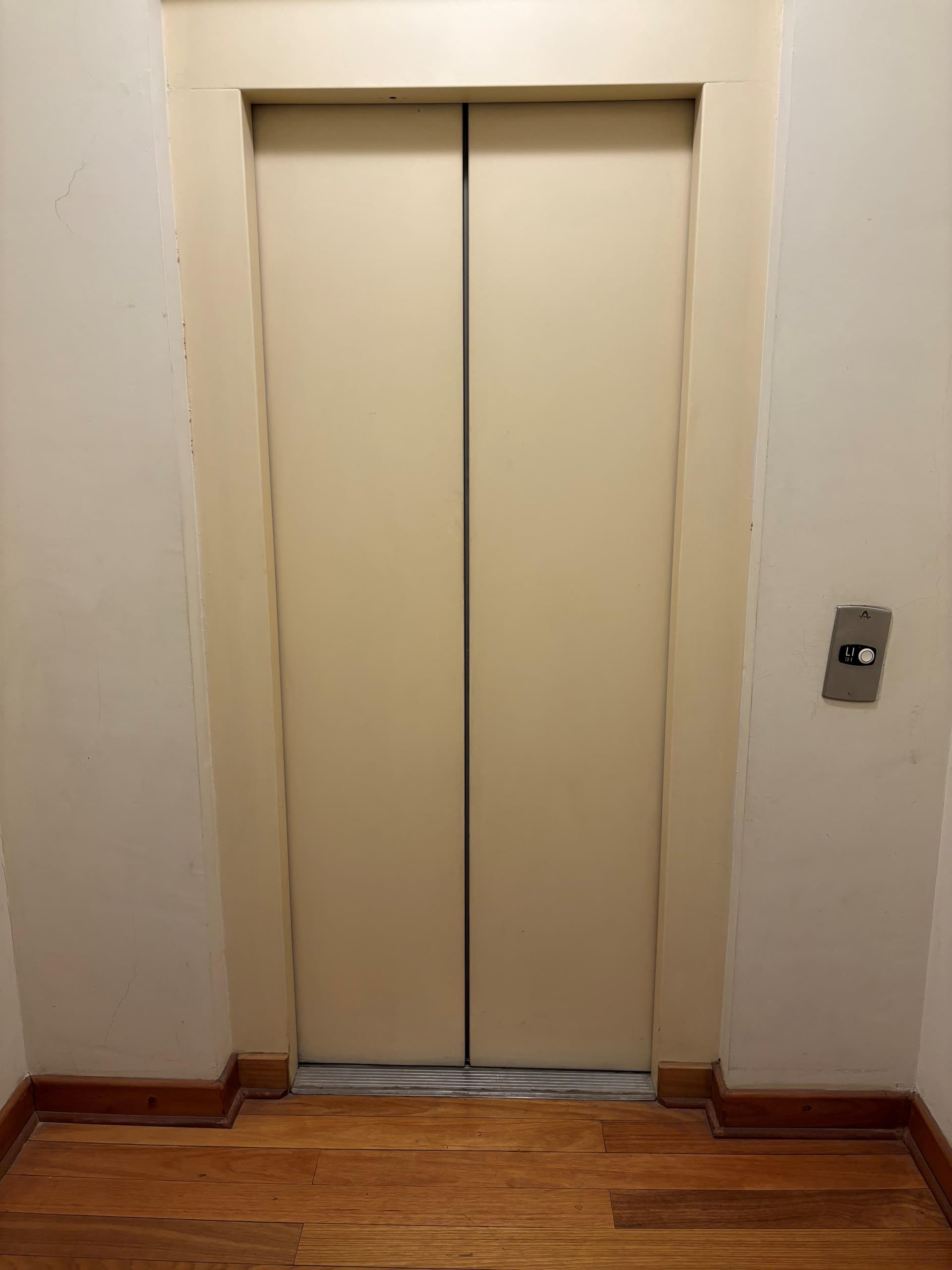 Puerta de ascensor en pasillo con piso de madera.
