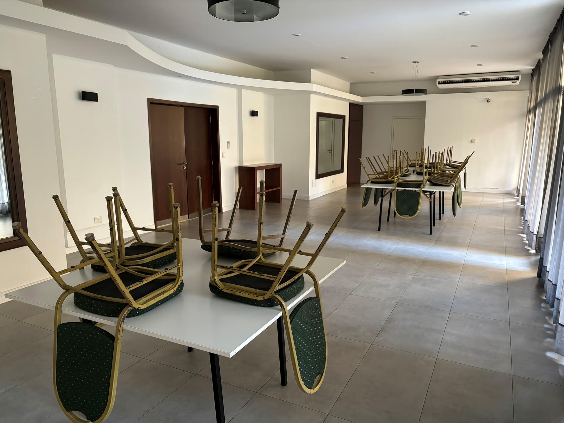 Salón de usos múltiples con mesas y sillas apiladas.