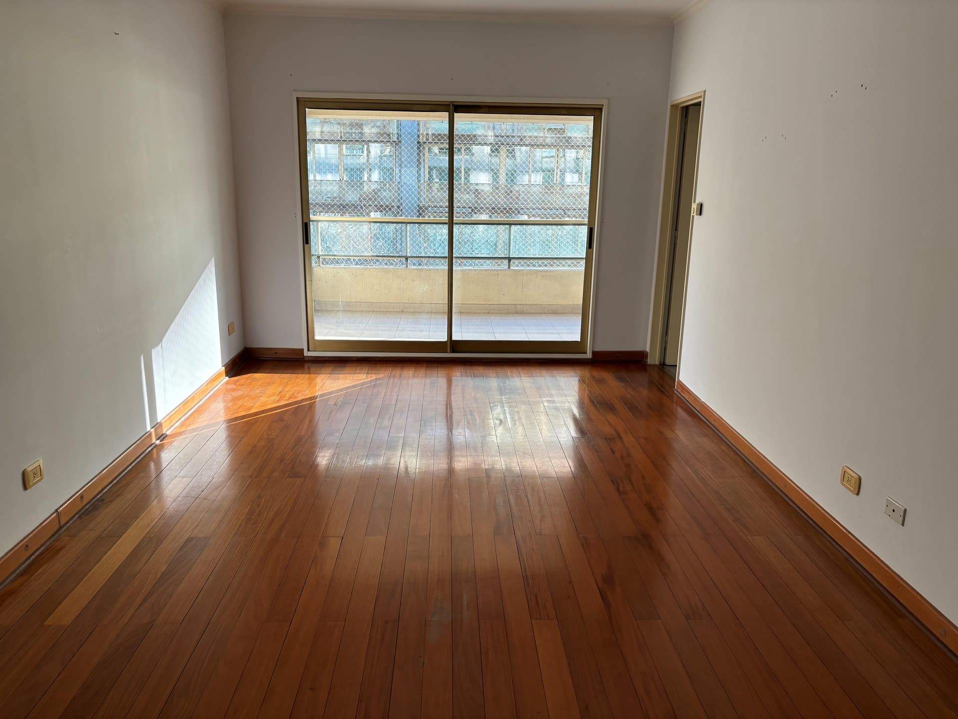 Living comedor vacío con piso de madera y salida al balcón.