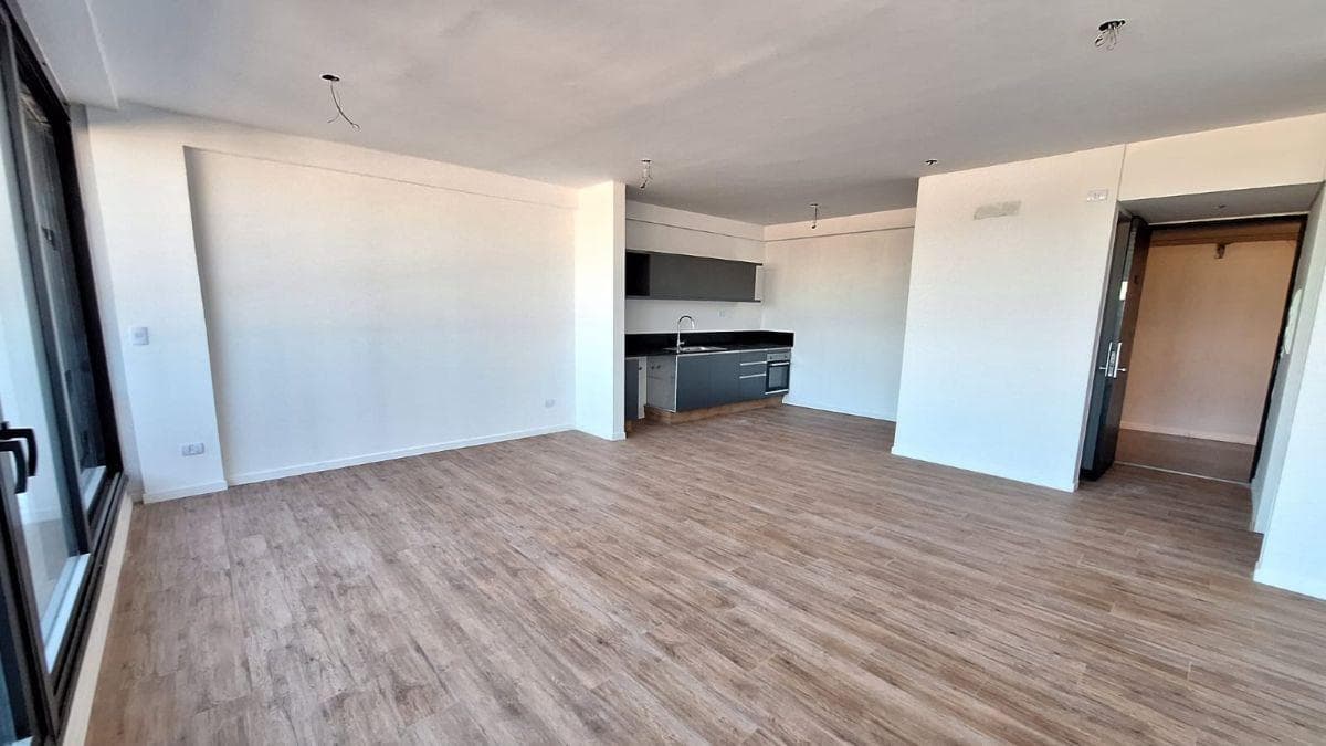 Amplio living comedor con cocina integrada, piso de madera y gran ventanal lateral.