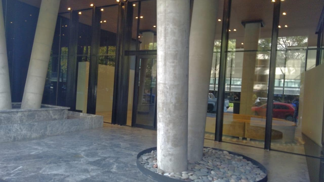 Entrada al edificio con columnas de hormigón y plantas decorativas.