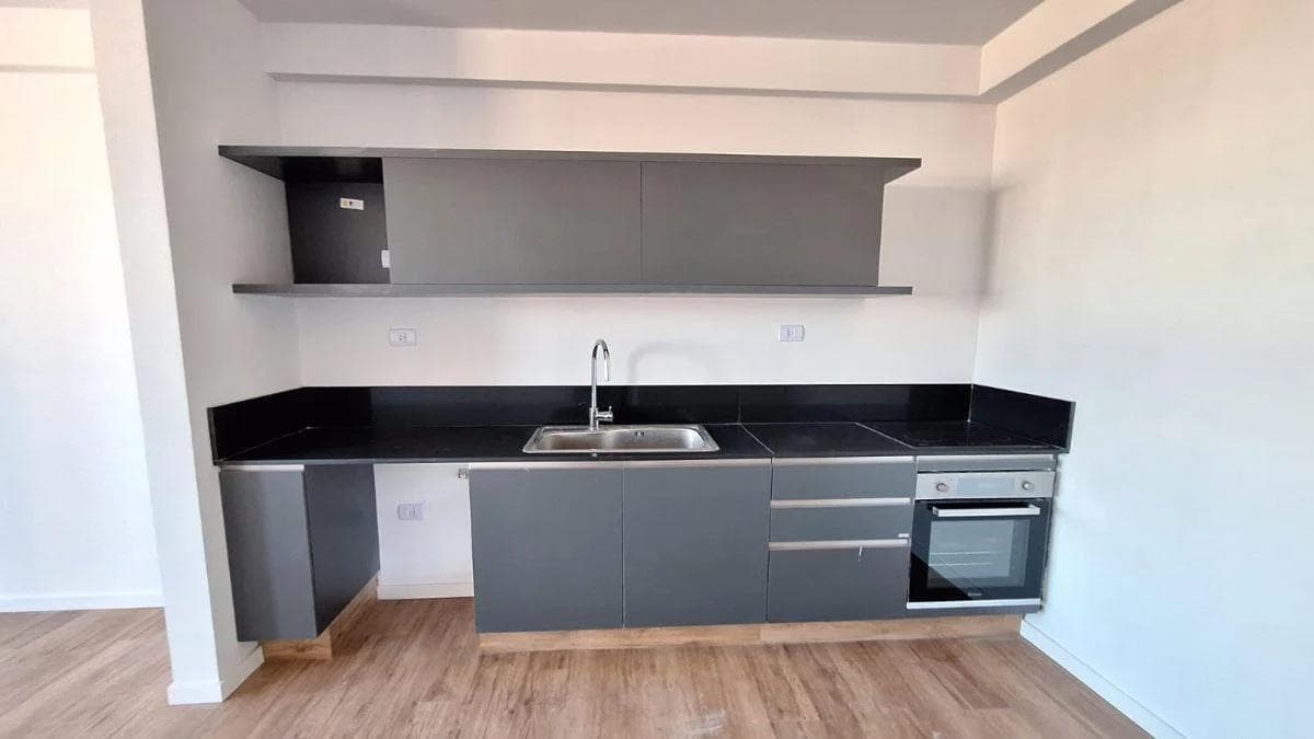 Cocina integrada con mesada oscura, bacha, anafe y alacenas grises.