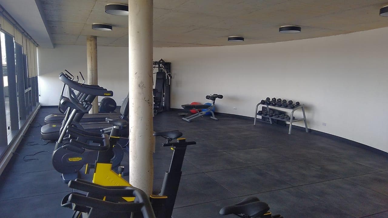 Gimnasio con máquinas de cardio y pesas en un rack metálico.