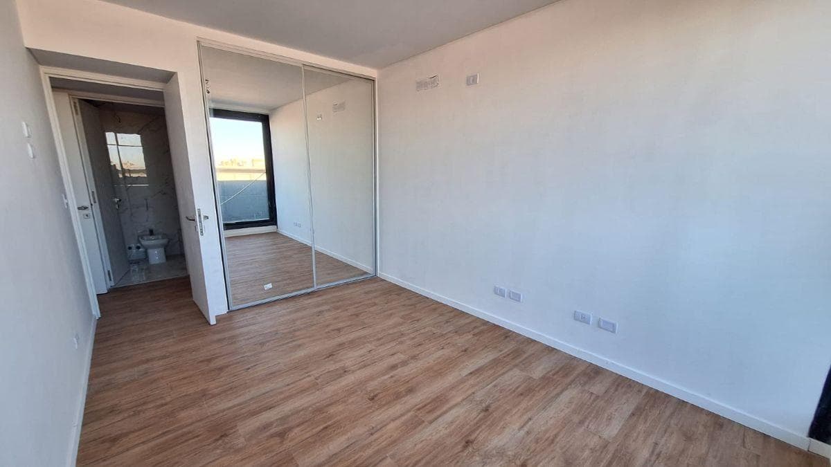 Dormitorio principal vacío con placard de puertas espejadas y baño en suite.