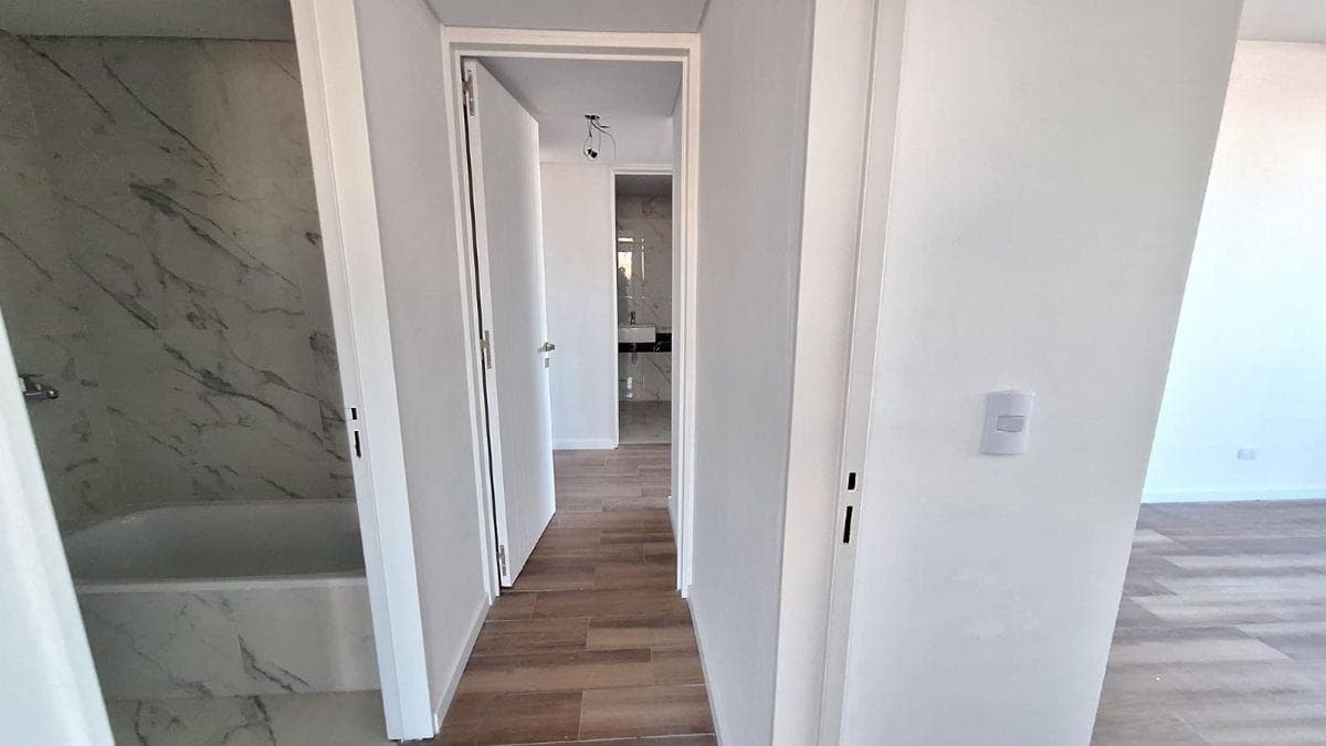 Pasillo de distribución con vista a un baño con bañera y bacha.