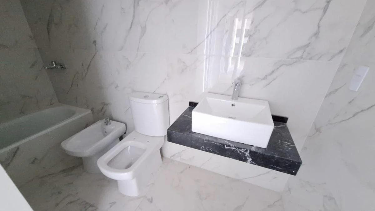 Baño con bañera, inodoro, bidet y vanitory, paredes de mármol blanco.