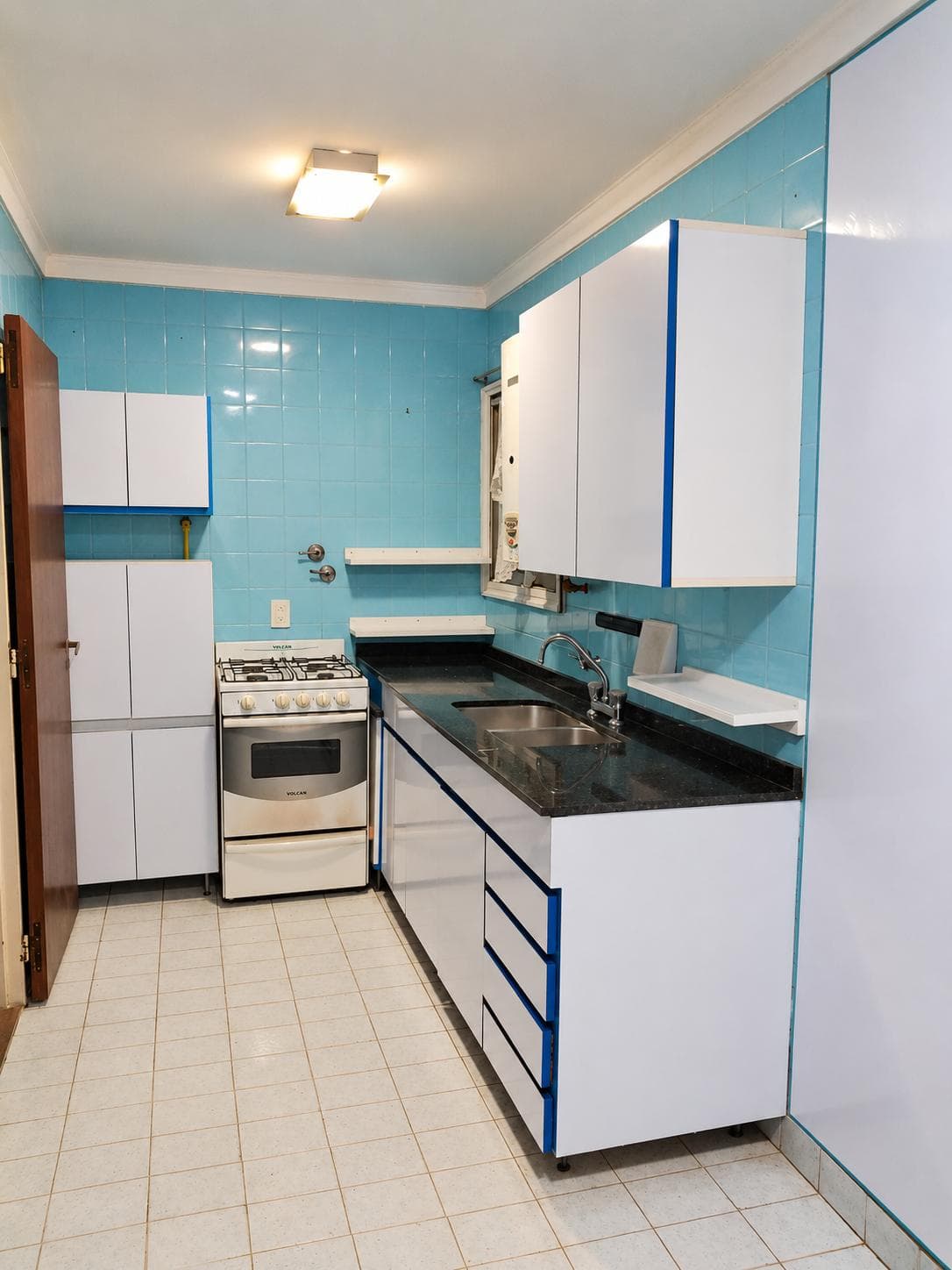 Cocina con azulejos azules, anafe, horno, termotanque y pileta doble.