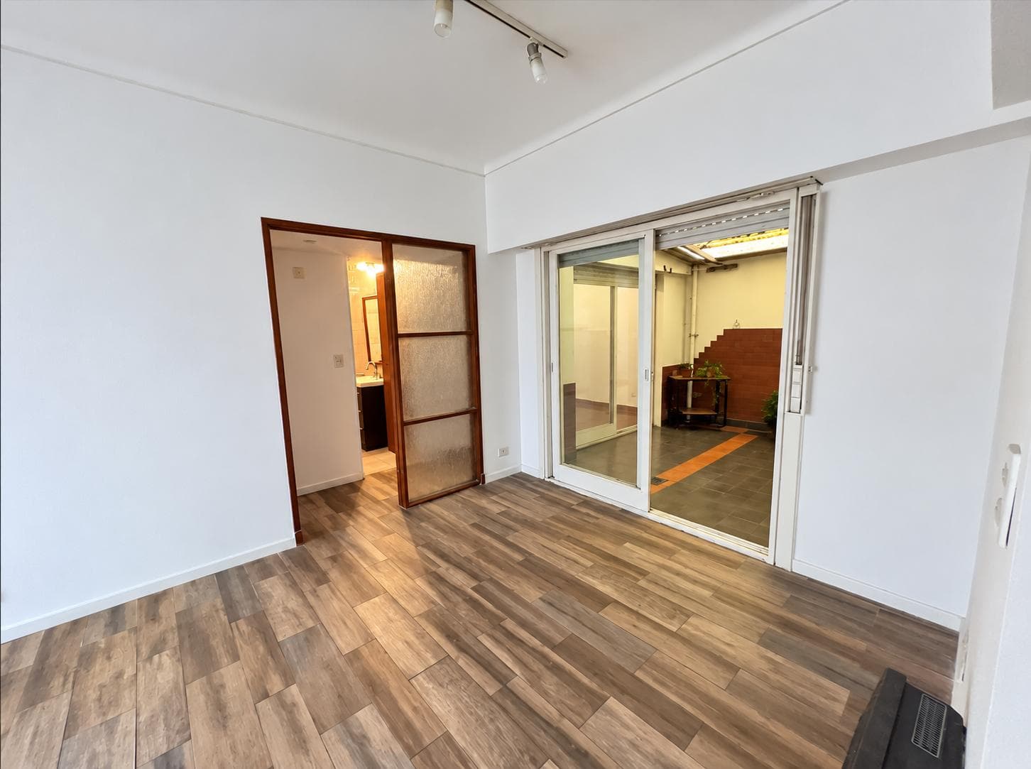 Living-comedor con piso de madera, puerta balcón hacia un patio y puerta de vidrio.