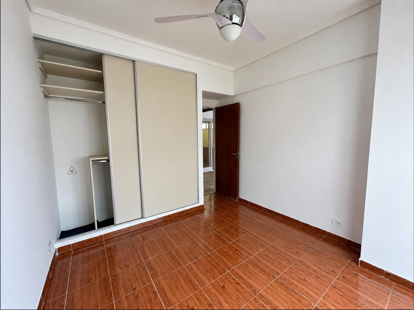 Dormitorio vacío con placard, ventilador de techo y piso de baldosas marrones.