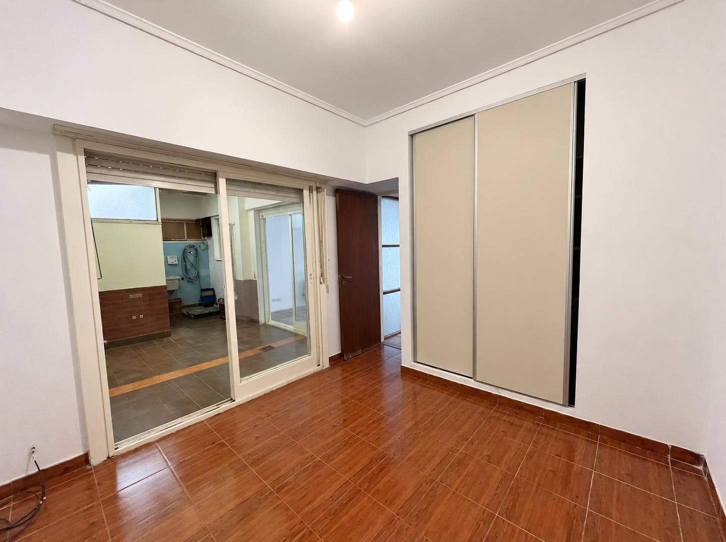 Dormitorio vacío con placard, ventilador de techo y puerta ventana a un lavadero.