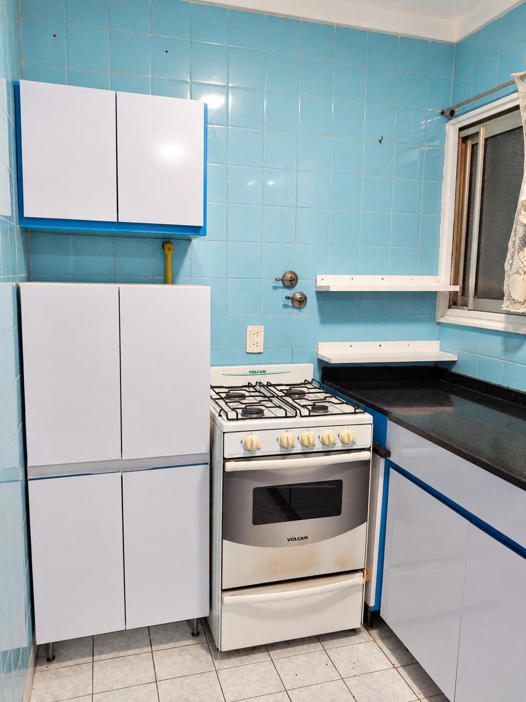 Cocina con azulejos azules, anafe a gas, horno y muebles blancos.