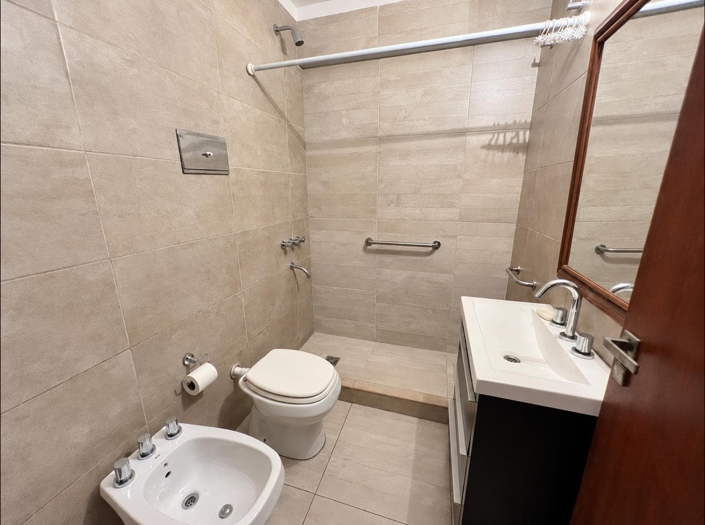 Baño completo con ducha a piso, inodoro, bidet y vanitory con espejo.
