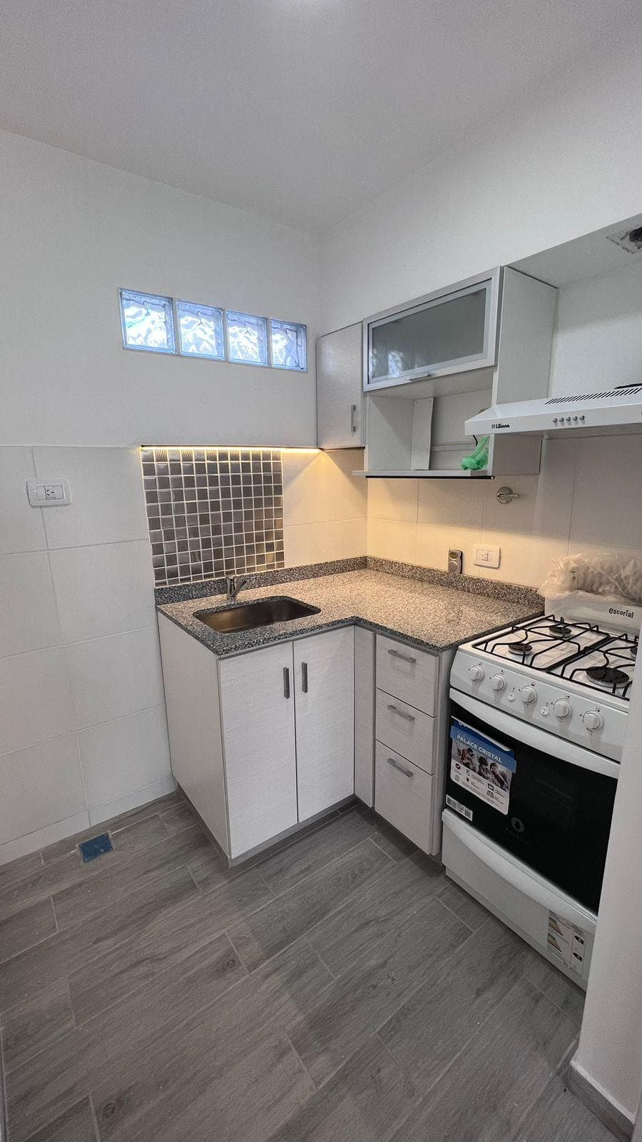 Cocina pequeña con mesada de granito, bacha, anafe y alacenas blancas.