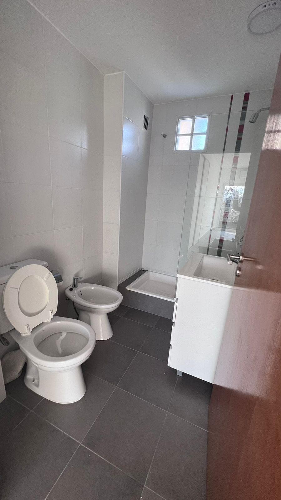 Baño completo con inodoro, bidet, vanitory y ducha con mampara de vidrio.