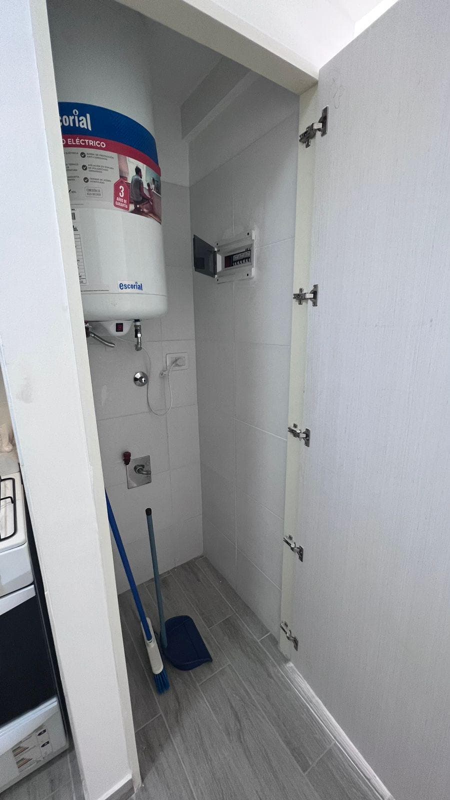 Lavadero pequeño con termotanque eléctrico y elementos de limpieza.
