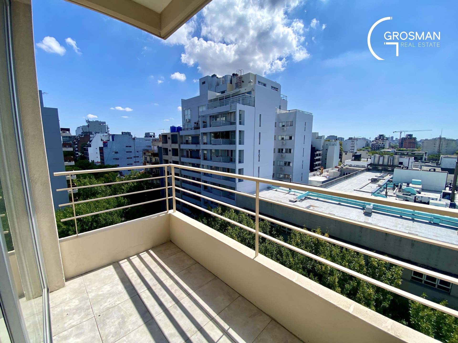 Balcón con baranda y vista a la ciudad con edificios y árboles.